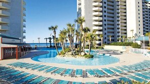 Un área de piscina en un resort con múltiples sillas de descanso y palmeras, rodeada de edificios altos.