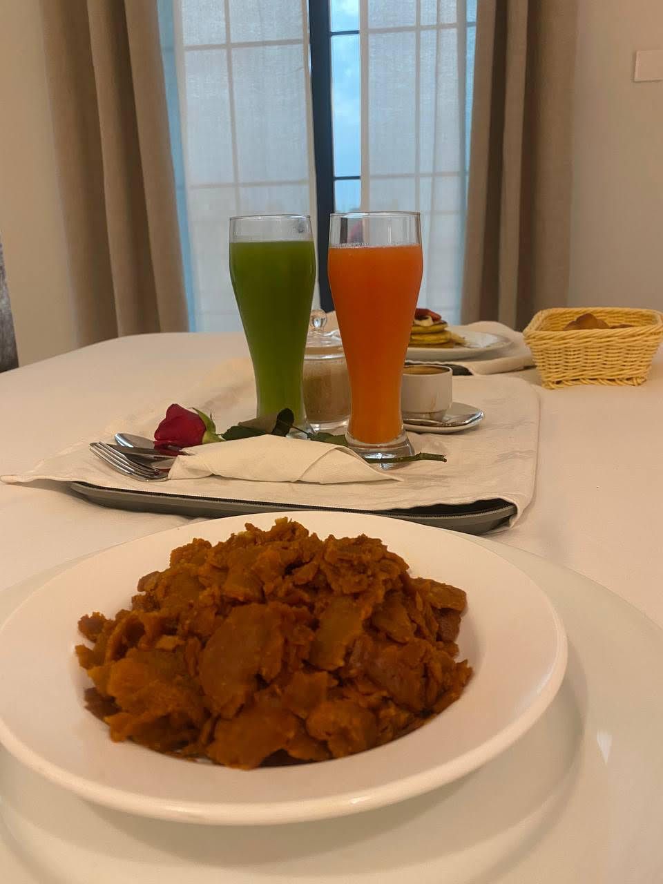 Un tavolo da pranzo con un piatto di cibo, due bicchieri di succo e una rosa su un tovagliolo.