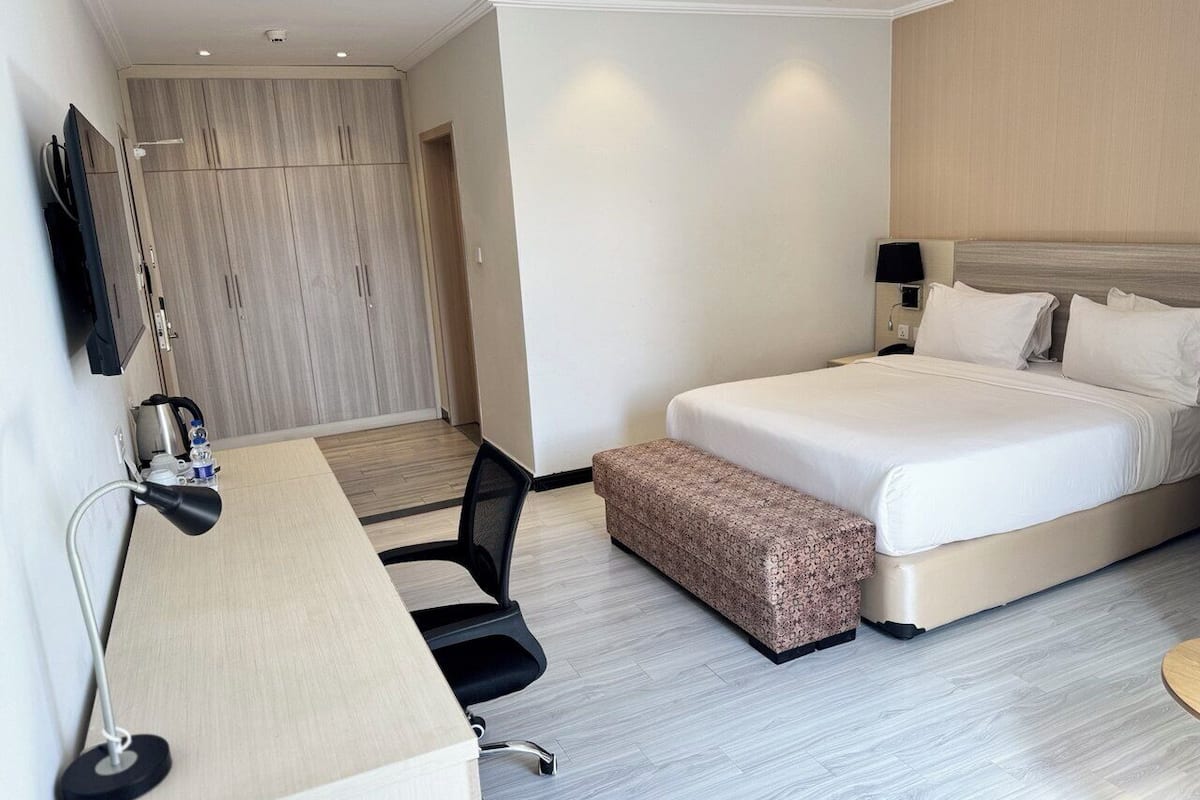 A hotel room with a bed, a desk, a chair, and a small bench.