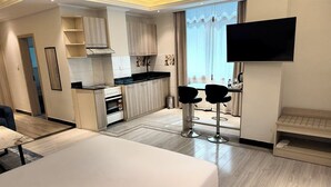 A modern hotel room with a large bed, a kitchenette, a TV mounted on the wall, and a view of the outdoors. - Bentark Hotel  (Addis Ababa)