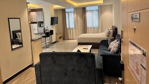 A hotel room with a sofa, a coffee table, a TV, and a bed. There is a kitchen area in the background. - Bentark Hotel  (Addis Ababa)
