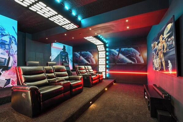 A cinema with red and black leather seating, a large screen, and space-themed wall art. - Amazing 10BR Jurassic World in Windsor Island (Davenport)