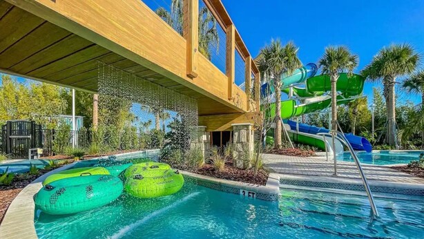 A swimming pool with two green inflatable tubes, a water slide, and a covered area with a wooden roof. - Brand New 10BR at Windsor Island/Pool/Spa/Firework View (Davenport)