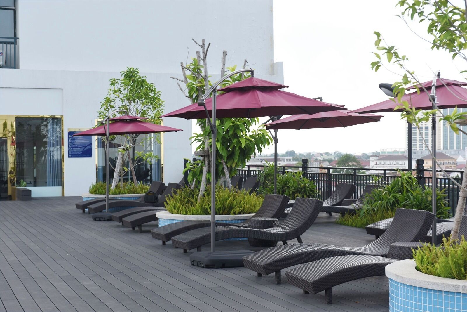 A rooftop lounge area with sun loungers, umbrellas, and potted plants.