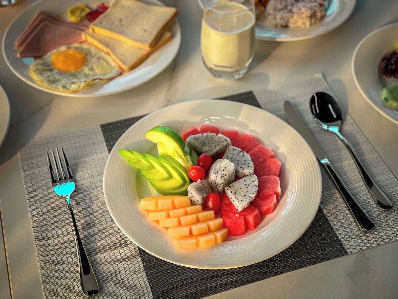 A breakfast plate with fruit and eggs, a glass of milk, and a sandwich on a table.