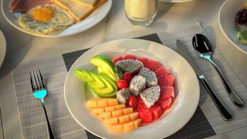 A breakfast plate with fruit and eggs, a glass of milk, and a sandwich on a table.