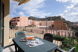 Un balcón con mesa lista para comer, con vistas a una zona residencial con edificios y una montaña al fondo.