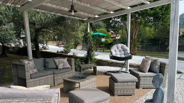 An outdoor patio area with wicker furniture, including sofas and chairs, a hanging chair, and a Buddha statue.