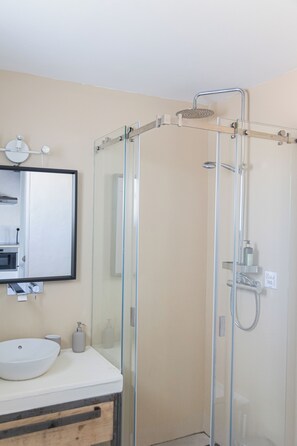Un bany modern amb plat de dutxa tancat per vidre, un lavabo blanc i un mirall sobre el lavabo.