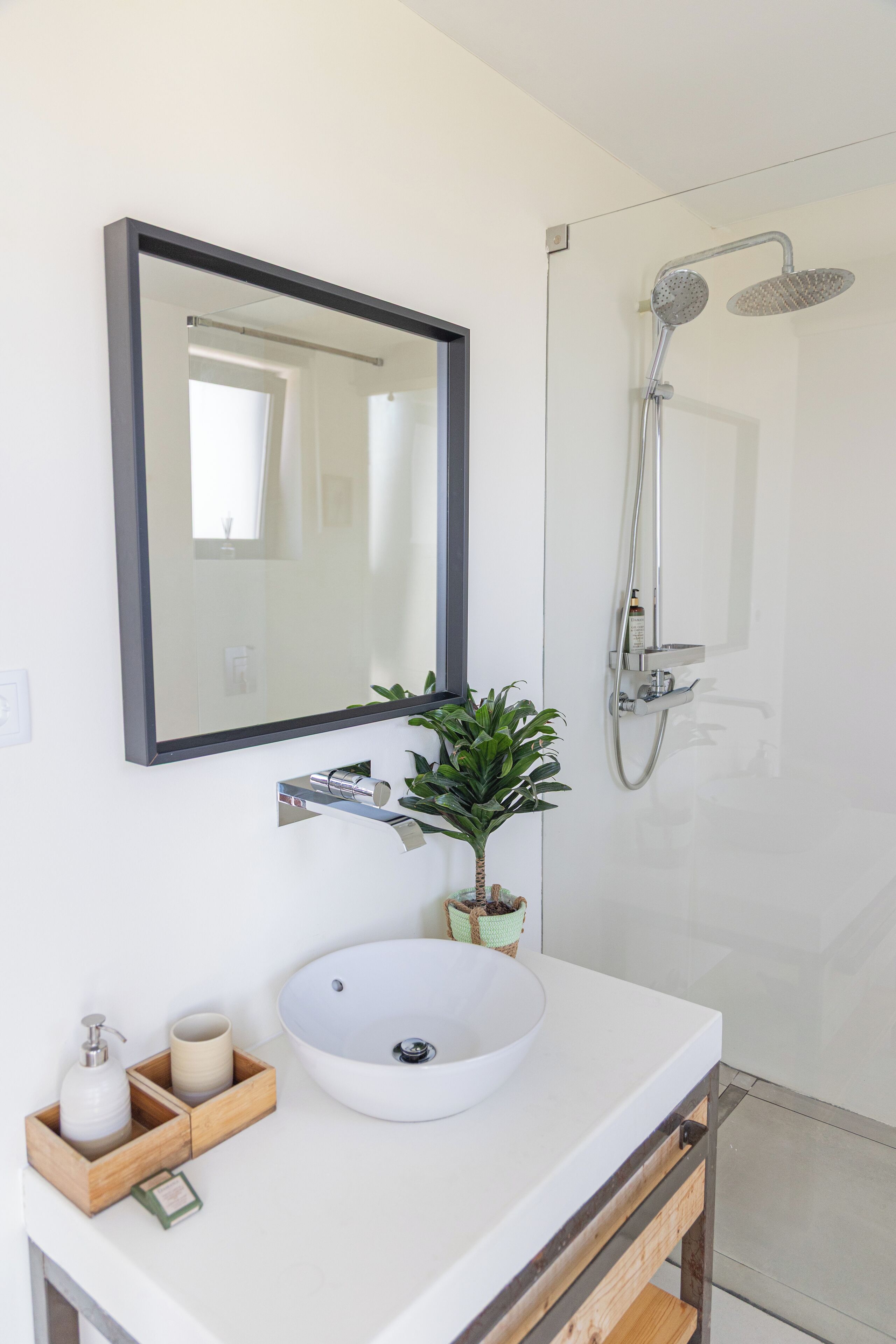 Un baño moderno con un lavamanos blanco, un espejo, ducha y una planta en maceta.