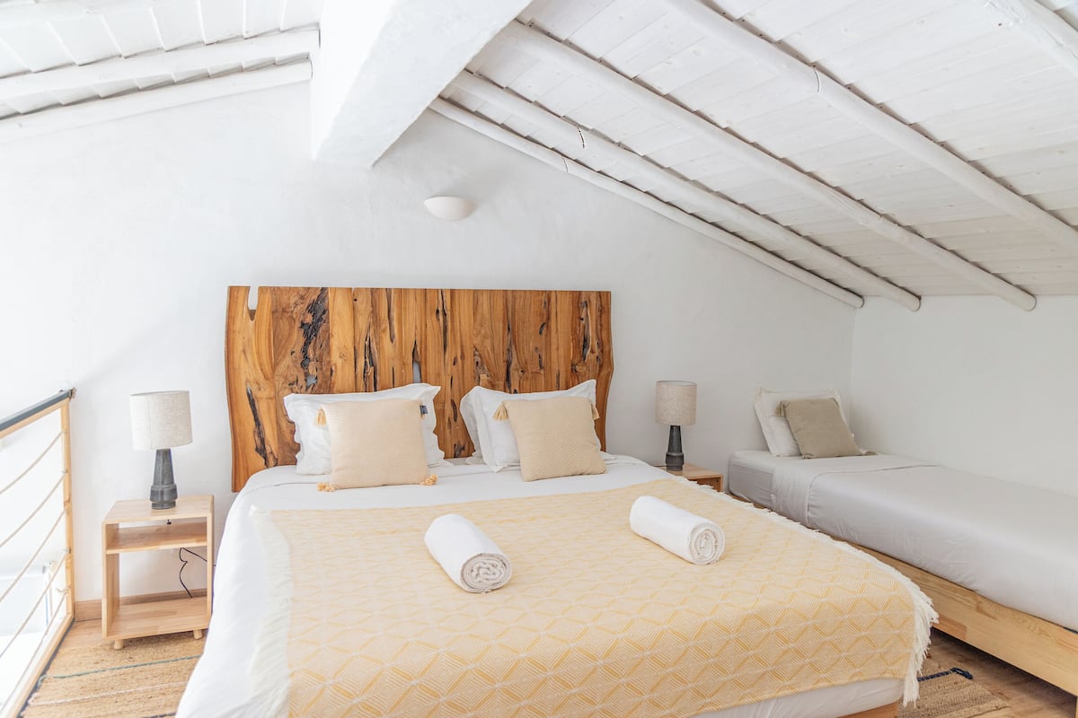 A bedroom with a wooden headboard, two beds, and a small bedside table with a lamp.