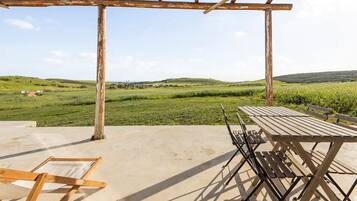 Une terrasse extérieure avec une table et des chaises en bois, une balançoire en bois et une vue sur des champs et des collines verdoyants.