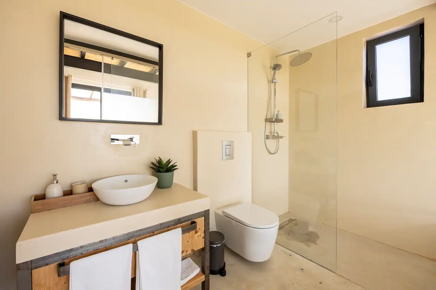 A modern bathroom with a large mirror, a vessel sink, a toilet, and a glass-enclosed shower.