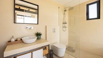 A modern bathroom with a large mirror, a vessel sink, a toilet, and a glass-enclosed shower.