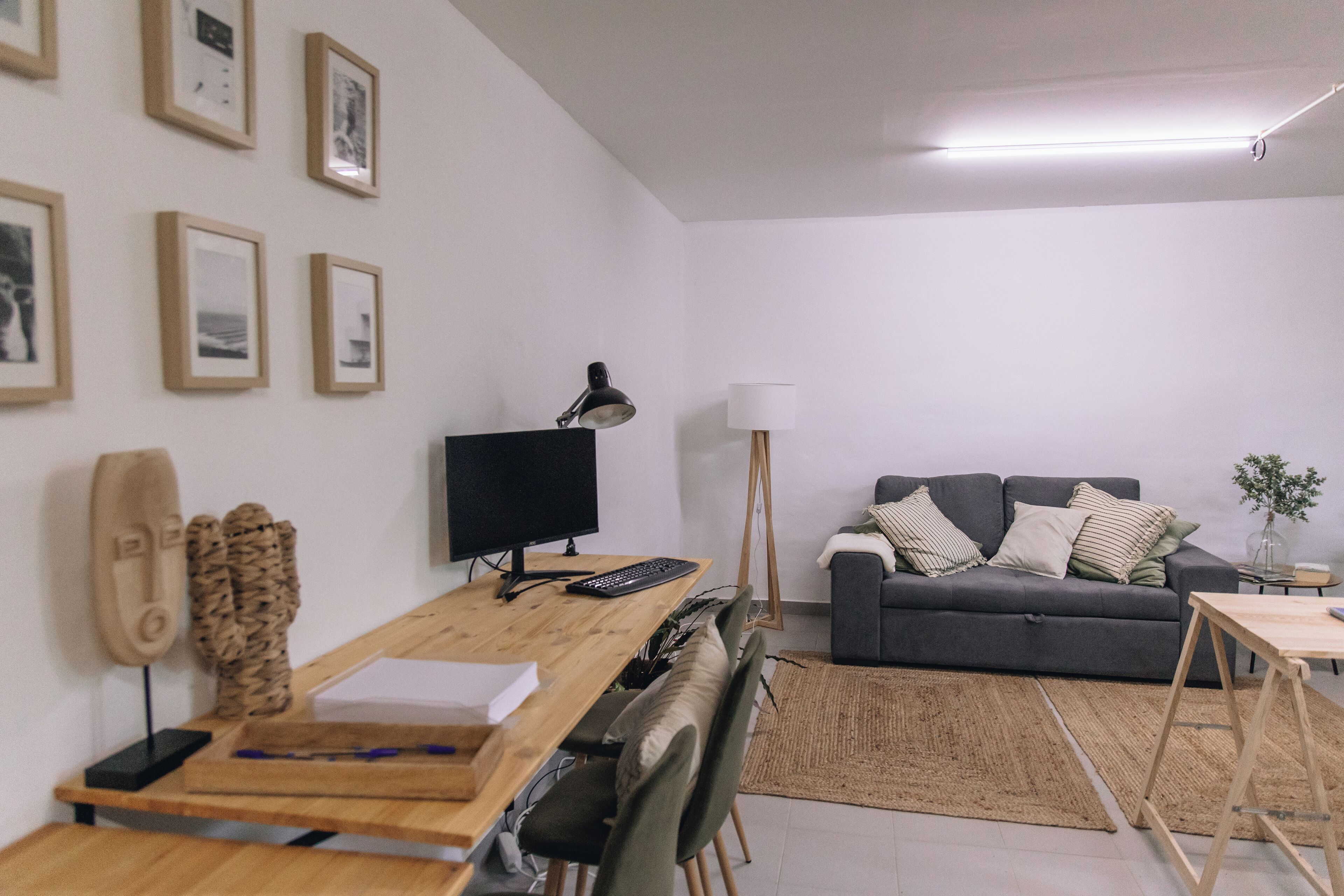 A modern living room with a wooden desk, a computer, a grey sofa, and a lamp.