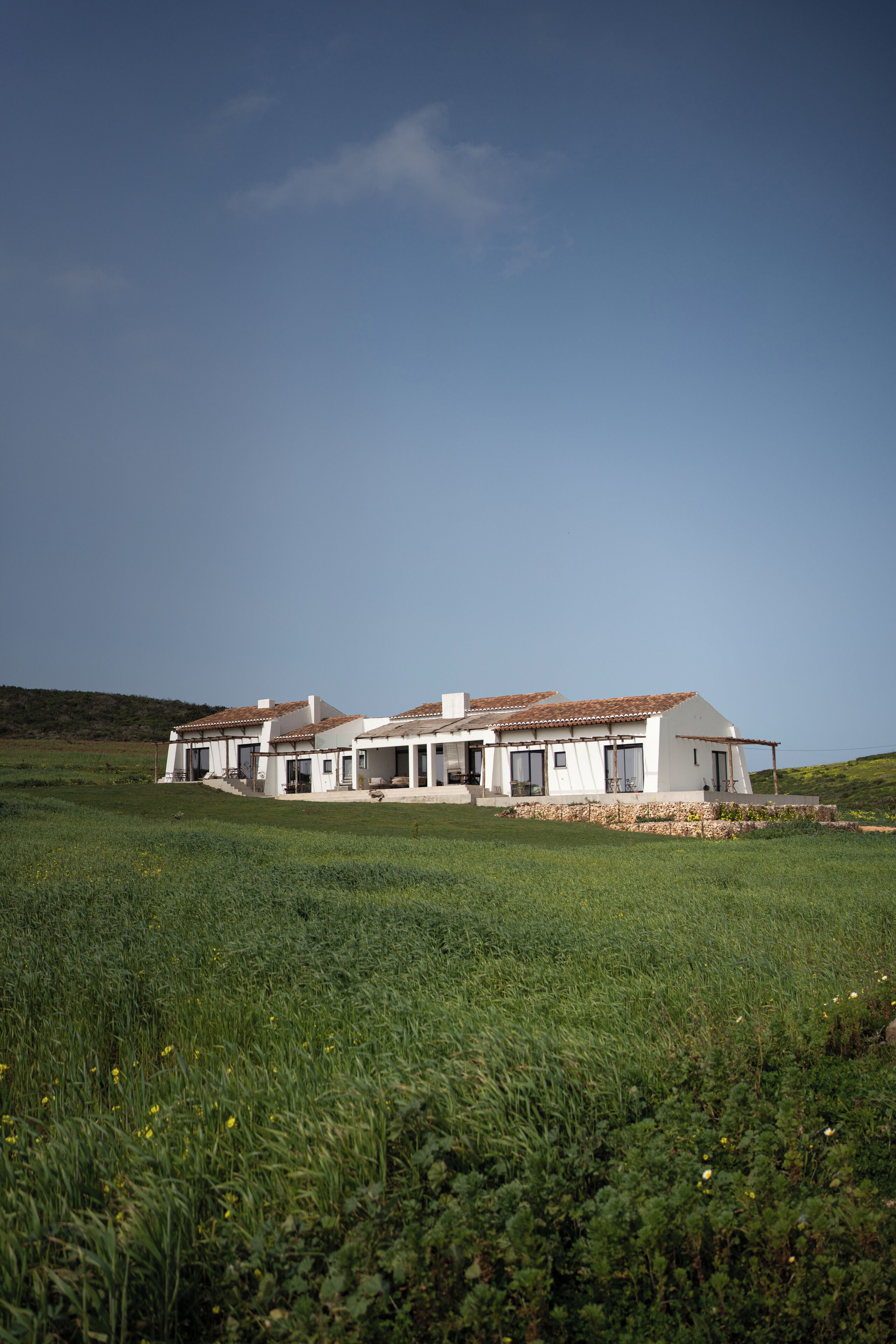 A white house with a tiled roof, surrounded by a grassy field.