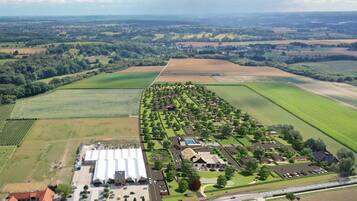 Luchtbeeld van een woongebied met een groot gebouwencomplex, groene velden en verspreide huizen.
