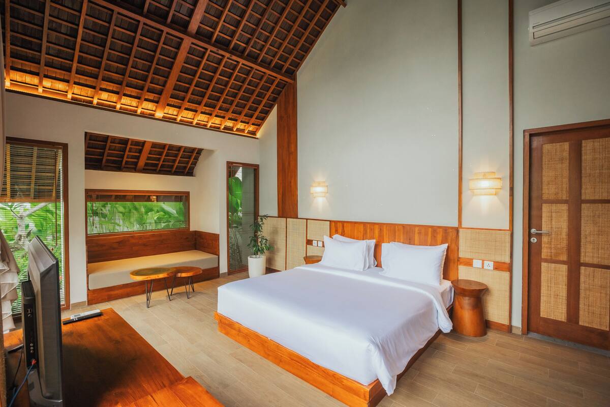 A modern bedroom with a large bed, wooden ceiling, and a view of greenery outside.