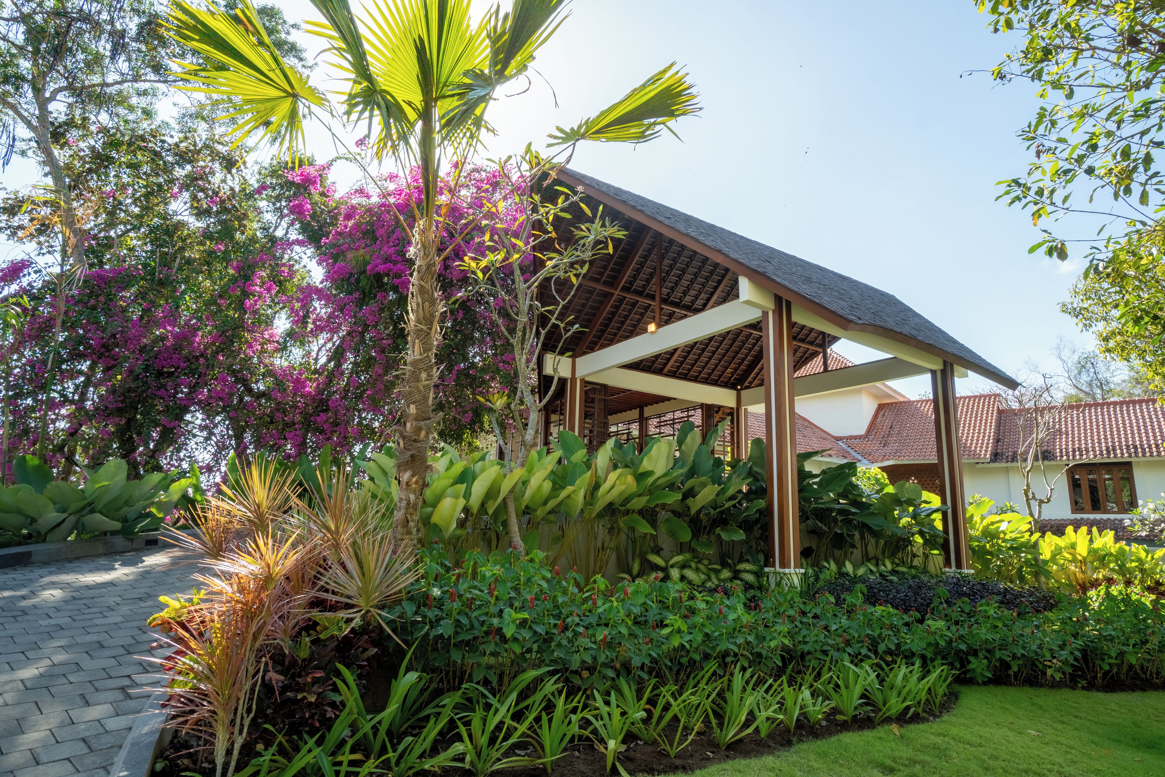 A covered outdoor area with a pergola, lush greenery, and flowering plants.