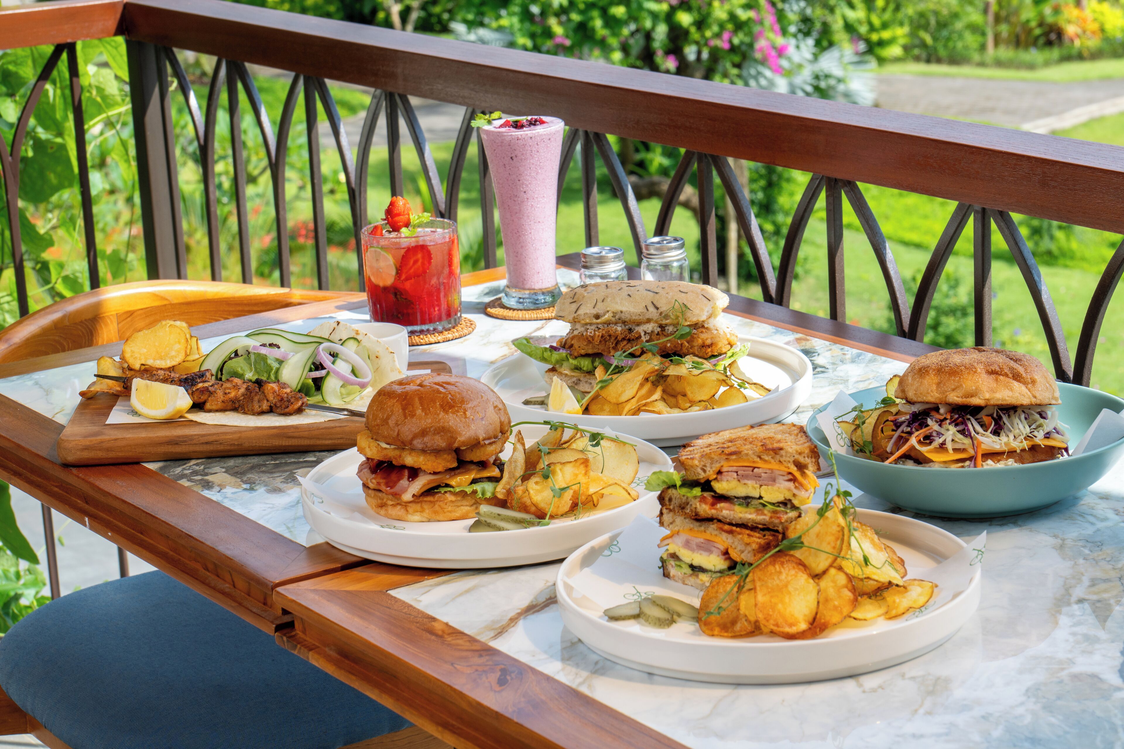 Ein Esstisch mit verschiedenen Gerichten, darunter Burger, Pommes und ein Smoothie.