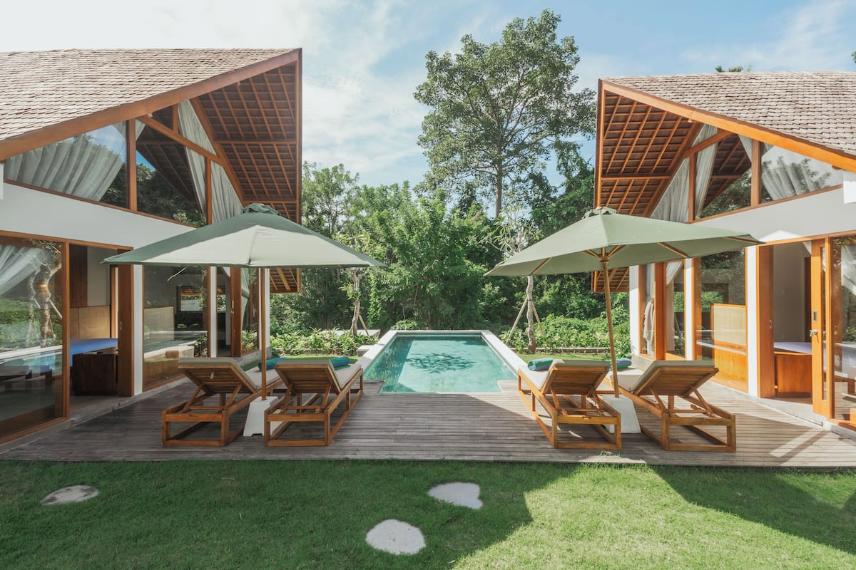 A modern outdoor pool area with wooden deck, lounge chairs, and umbrellas.