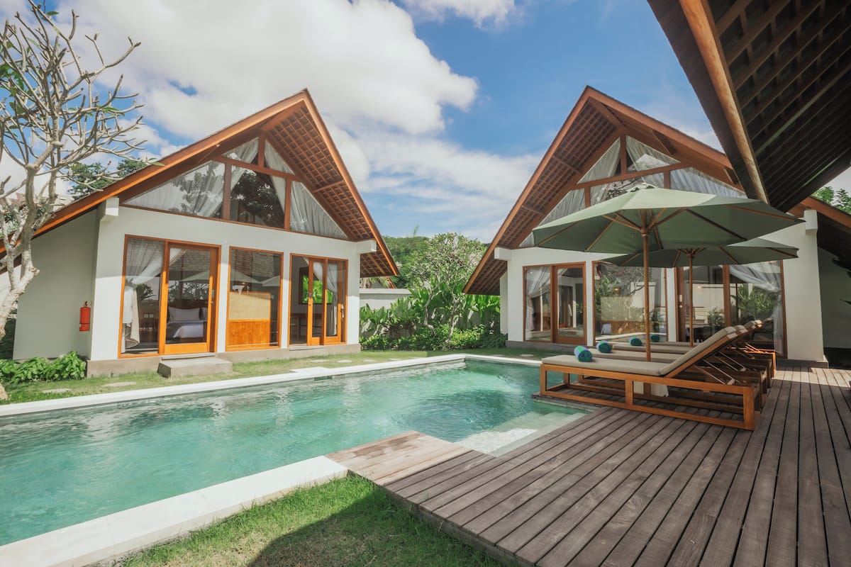 A modern resort with two guest villas, a swimming pool, and a wooden deck with lounge chairs.