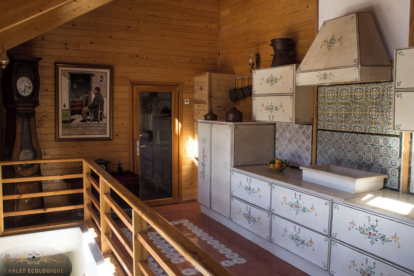 Ein rustikales Holzinnenambiente mit einer Holztreppe, einer Küche mit weißen Schränken, einer gefliesten Spritzschutzleiste und einem gerahmten Bild an der Wand.