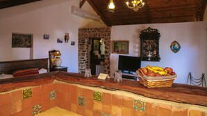 A rustic interior with a wooden ceiling, a stone wall, a tiled bar area, and a television. - Dar Zaghouan (Zaghouan)