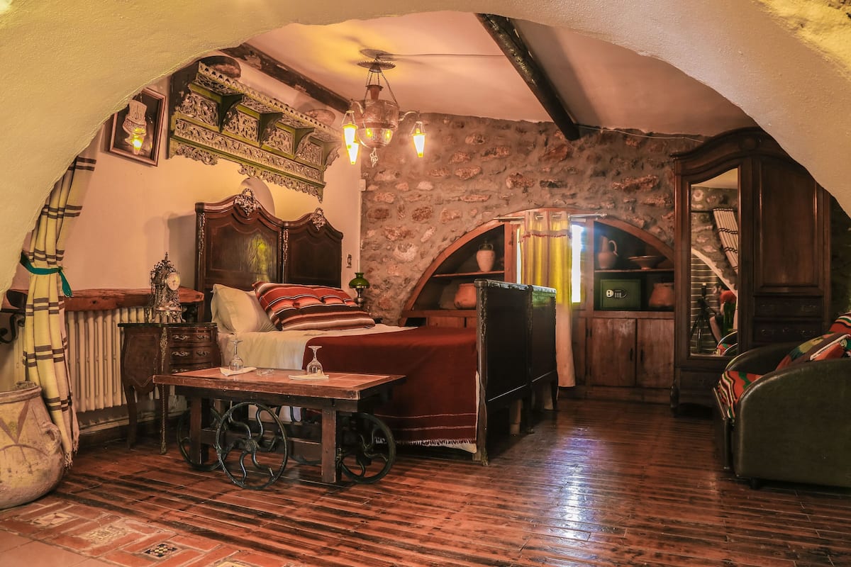 Una habitación acogedora con una cama de madera, una mesa con una copa de vino y un muro de piedra.