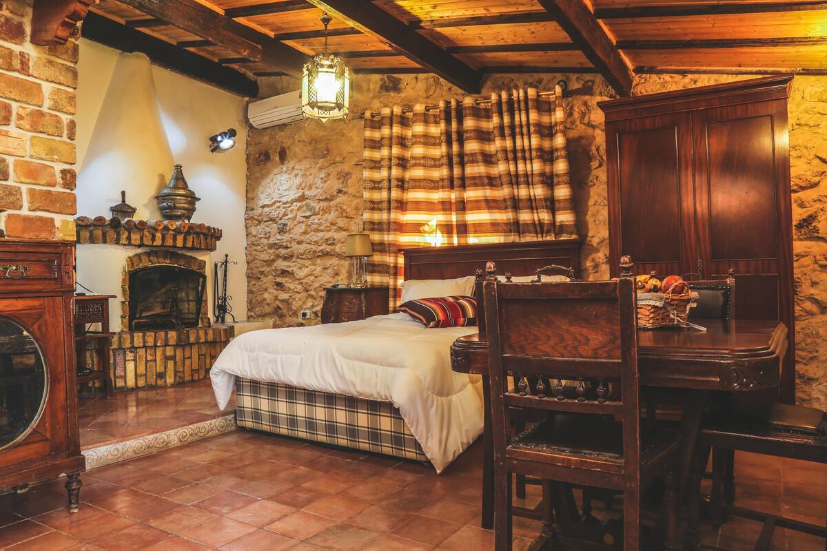 Un dormitorio rústico con cama, muebles de madera, chimenea y pared de piedra.