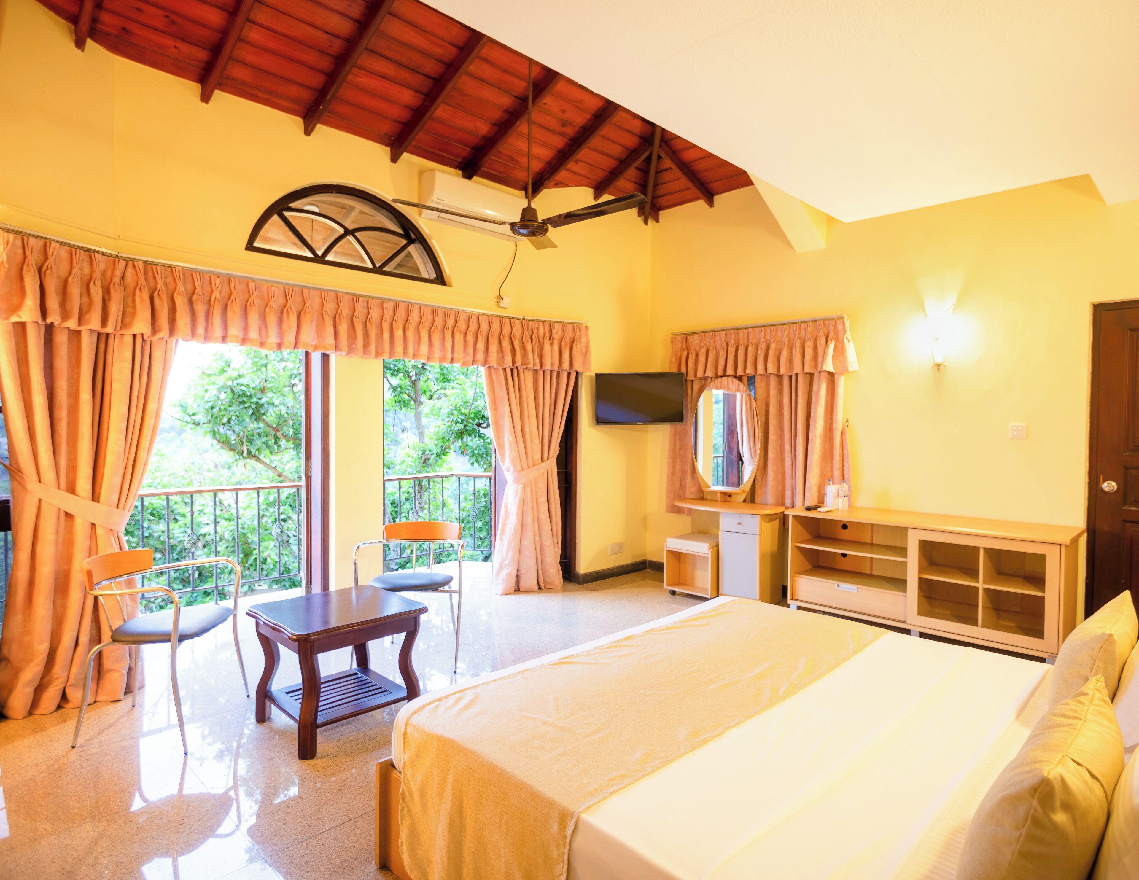 A hotel room with a bed, a desk, a chair, a TV, and a balcony with curtains.