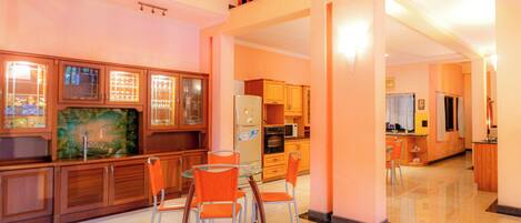A spacious kitchen with wooden cabinets, a dining area with orange chairs, and a large window overlooking the city.