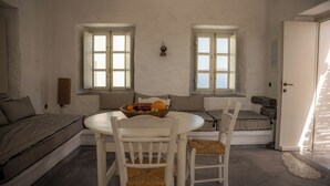 A room with a round table, two white chairs, a sofa, and a small window. - Experience your personal leap into time on Therasia island (Thirasia)