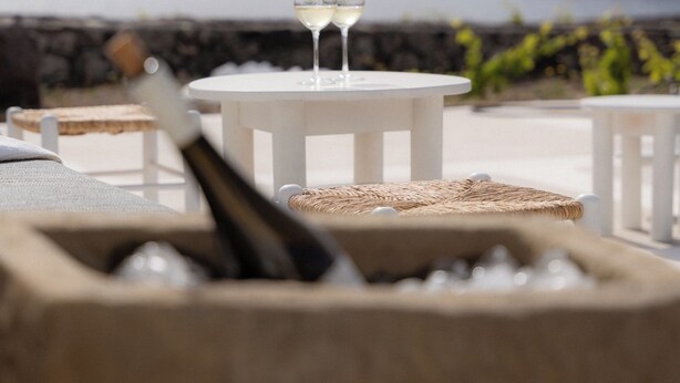 A seaside terrace with white tables and chairs, two glasses of white wine, and a bottle of champagne. - Experience your personal leap into time on Therasia island (Thirasia)