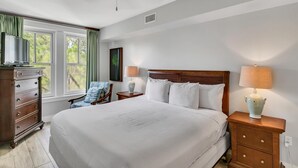 Une chambre à coucher bien rangée, avec un grand lit, une commode, une chaise et une table de chevet avec des lampes.