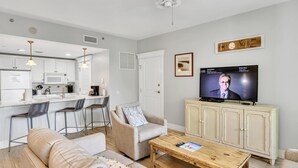 Un salon moderne avec un canapé, une table basse, un téléviseur et une cuisine en arrière-plan.