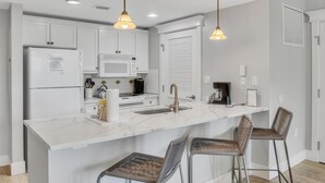 Une cuisine moderne avec des meubles blancs, un plan de travail en marbre et deux tabourets de bar en osier.