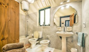 A bathroom with a bathtub, two toilets, a bidet, a sink, a mirror, and a towel rack. - Retro Designer Homelike Apartment - Close to Beach (Munxar)