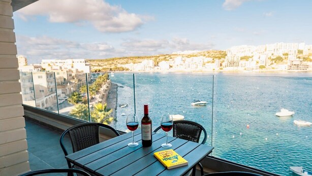 A balcony with a table, two wine glasses, a bottle of wine, and a book titled "And Then I Turned Into A Mermaid". - Seaside Magic From a Stunning Apartment (St. Paul's Bay)