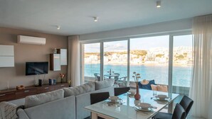 A modern living room with a sofa, TV, and dining area with a table set for two. - Seaside Magic From a Stunning Apartment (St. Paul's Bay)
