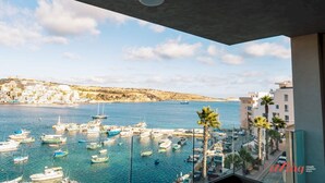 A marina with boats, a clear sky, and a coastal town in the background. - Seaside Magic From a Stunning Apartment (St. Paul's Bay)