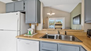 A kitchen with grey cabinets, a white refrigerator, a wooden countertop, a sink, and a window with a view of buildings.