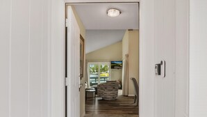 A hallway with a view into a living area, a fireplace, and a door leading to another room.