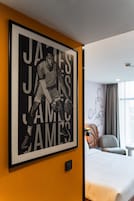 A framed poster of a basketball player on a hotel wall, a bed, and a window with curtains.