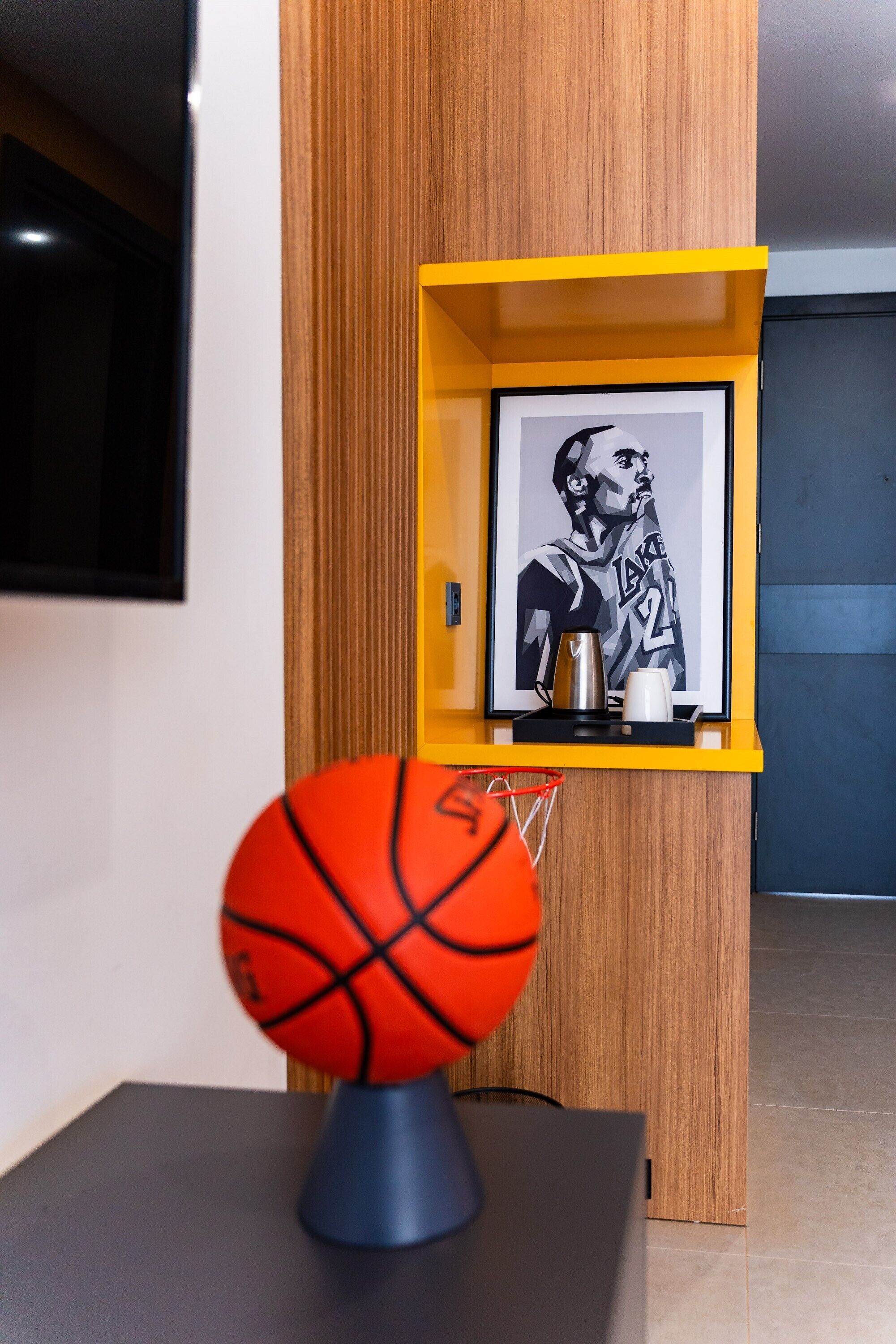 Un balón de baloncesto sobre un soporte en una habitación con un armario de madera y un cuadro en una estantería.