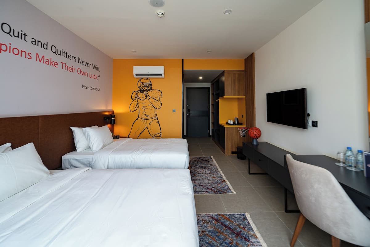 A hotel room with two beds, a desk, a chair, a TV, and a motivational quote on the wall.