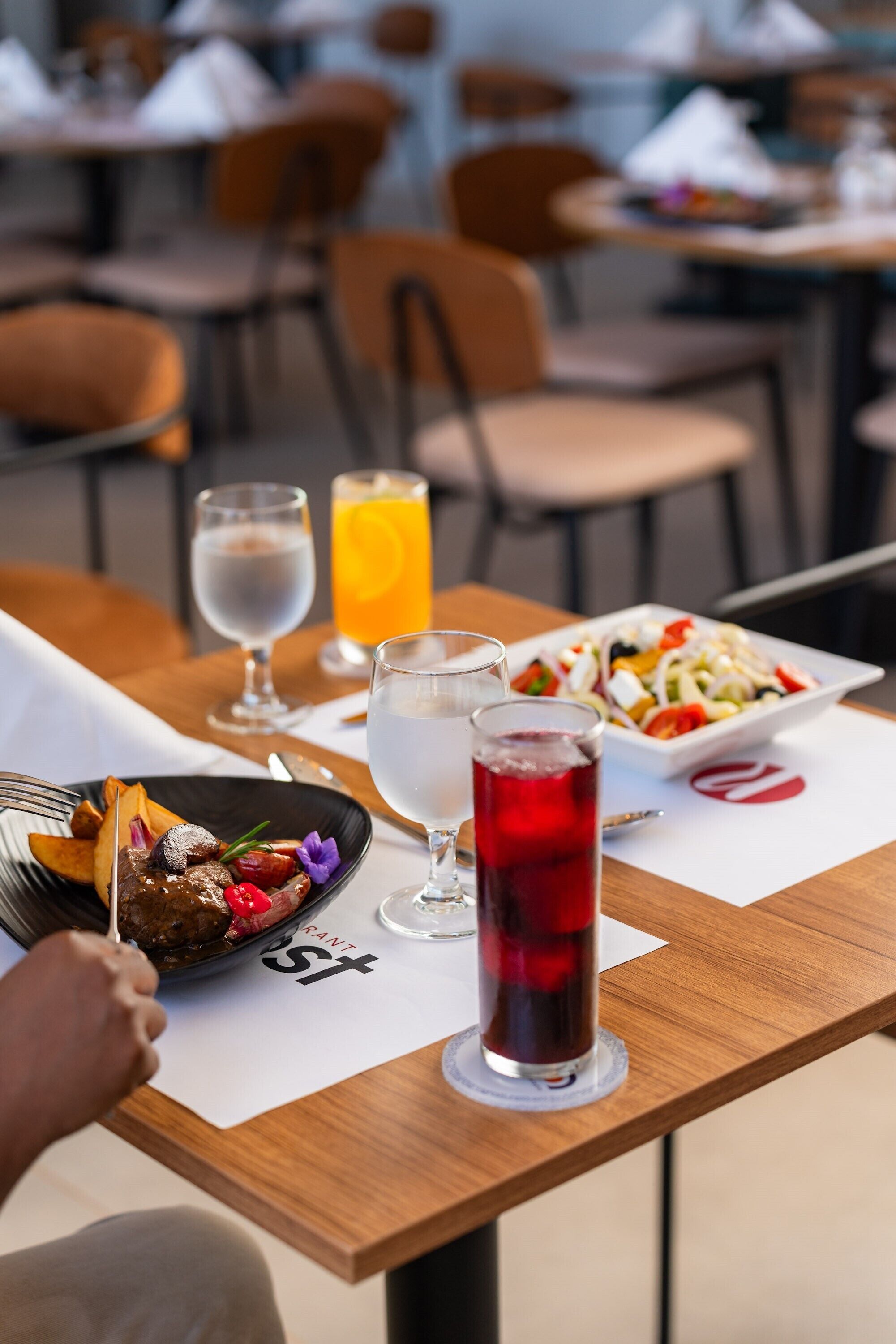 Une table à manger avec une assiette de nourriture, un verre de boisson rouge et un verre d’eau.