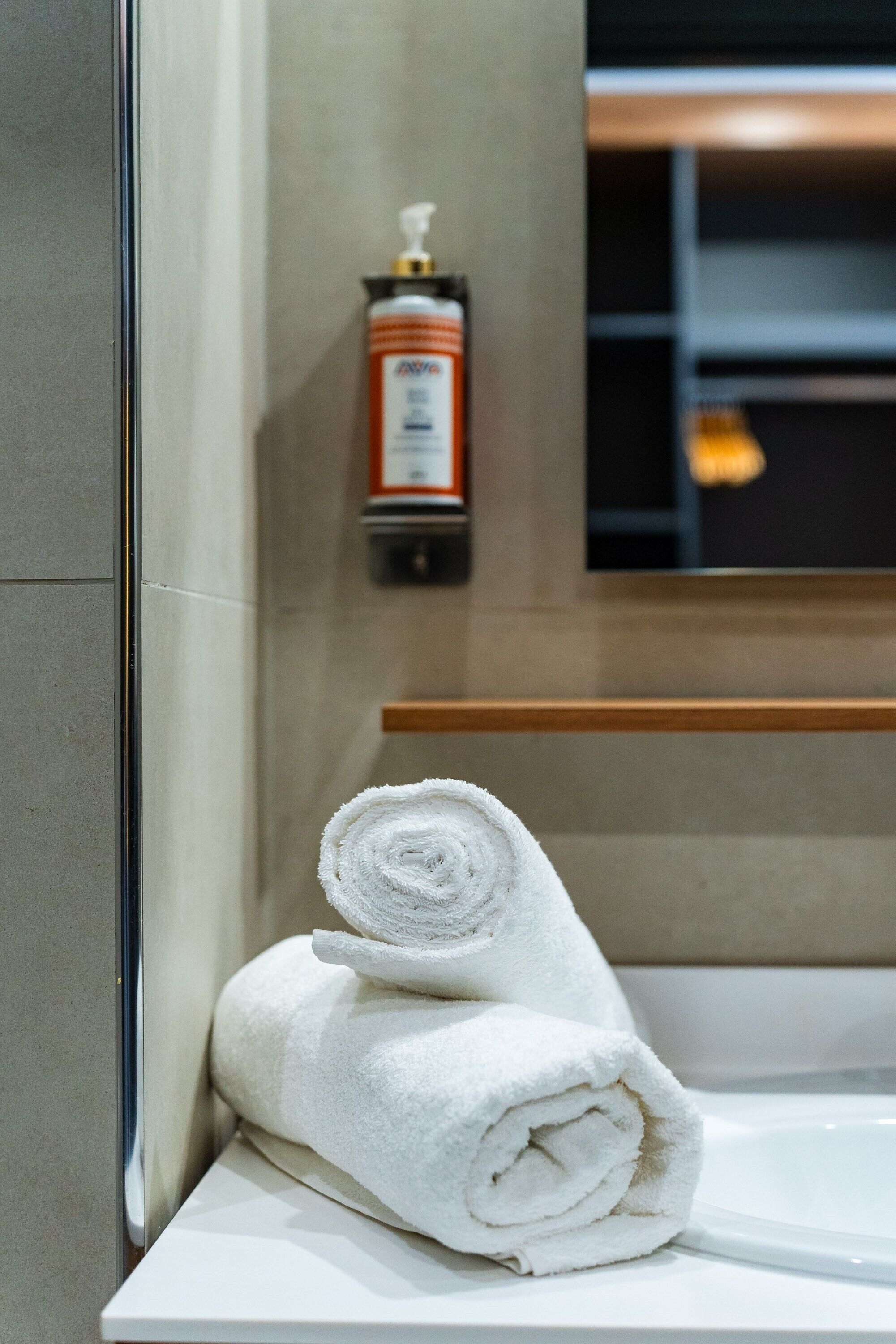 A bathroom with a white towel rolled up on a white sink.