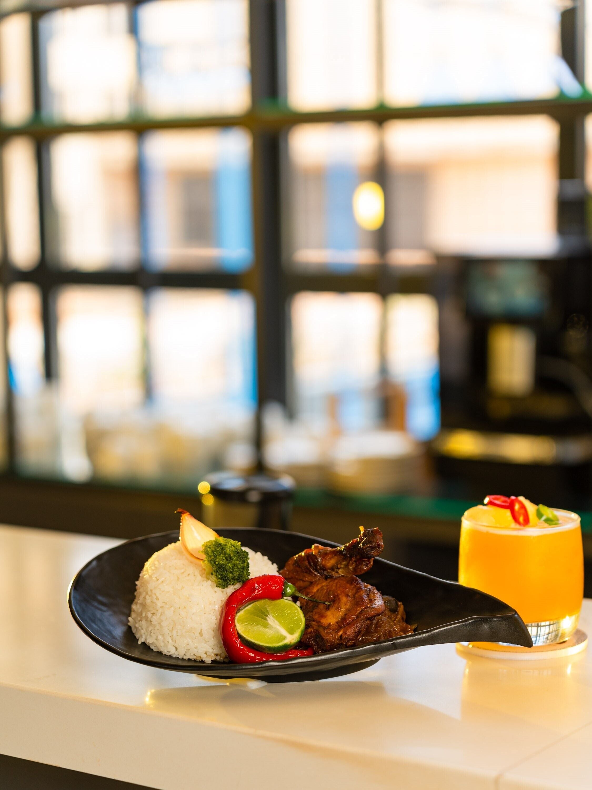 A plate of food with rice, vegetables, and meat, and a glass of orange juice on a table.