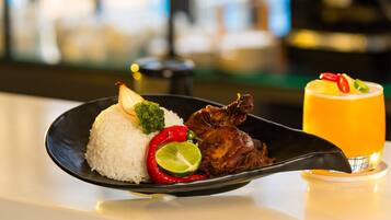 A plate of food with rice, vegetables, and meat, and a glass of orange juice on a table.